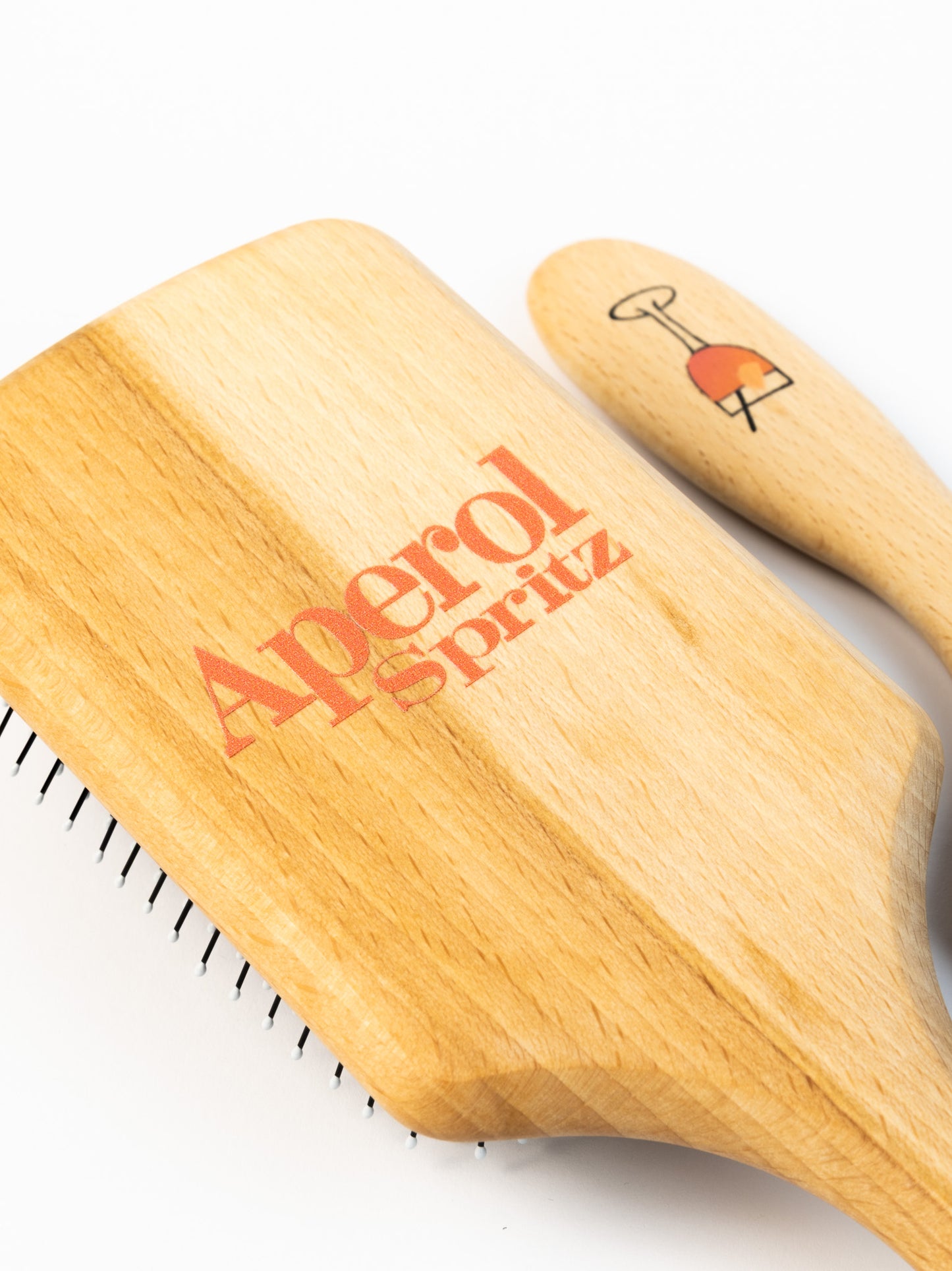 Nahaufnahme einer Haarbüste aus Holz mit einem Aperolglas auf dem Stiel aufgedruckt und Aperol Spritz Schriftzug auf dem Rücken.