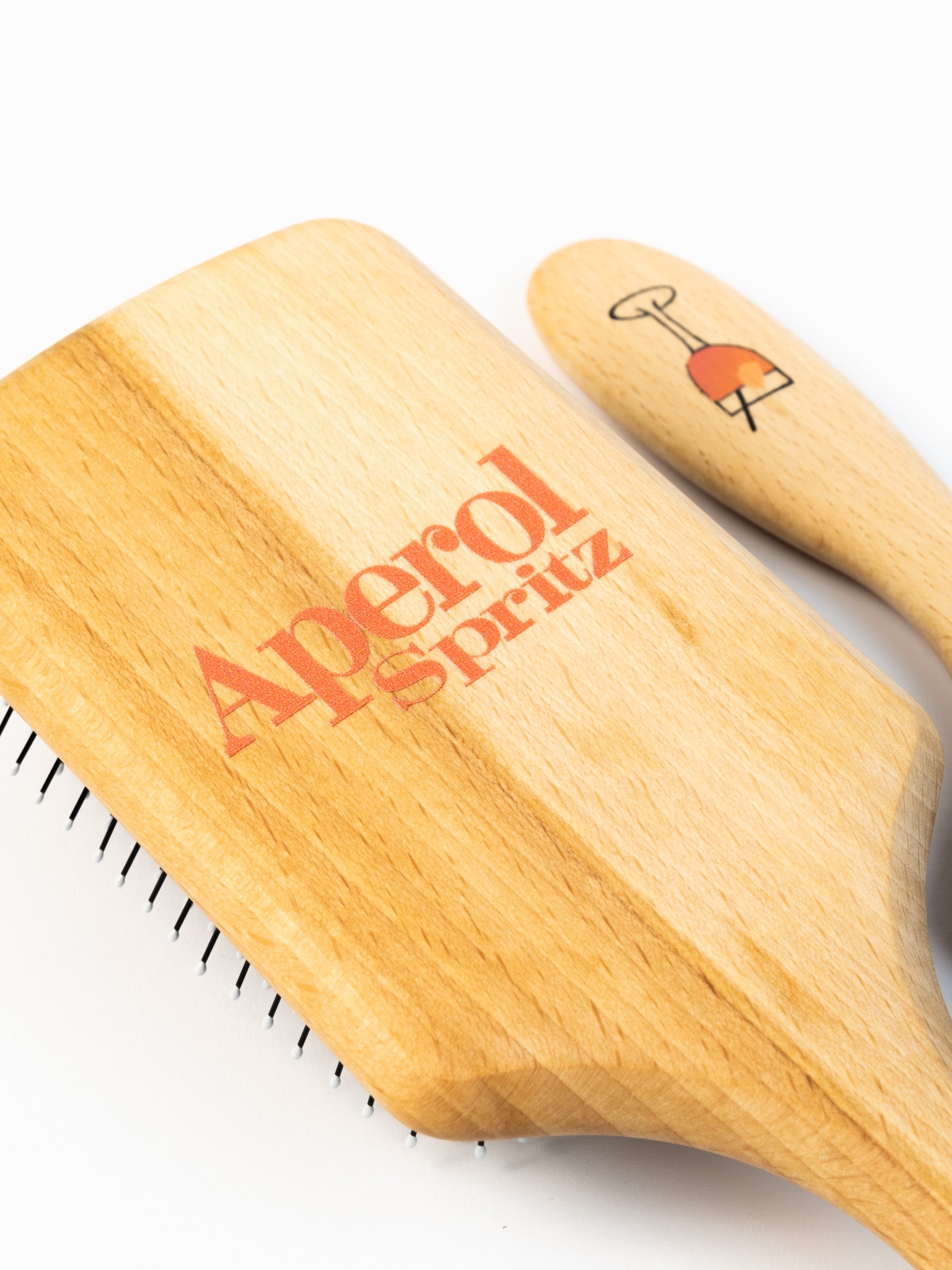 Nahaufnahme einer Haarbüste aus Holz mit einem Aperolglas auf dem Stiel aufgedruckt und Aperol Spritz Schriftzug auf dem Rücken.
